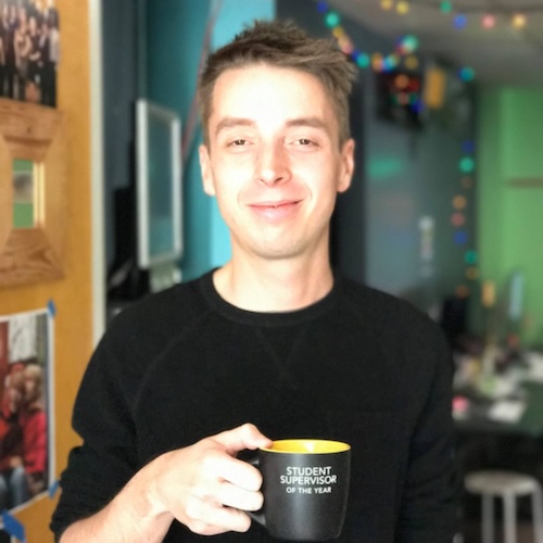 Dustin holding a 'Student Supervisor of the Year' coffee mug.